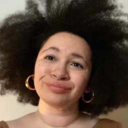 Headshot of Dorothy Berry, a person with light brown skin and an afro blowout wearing gold hoop earrings and a brown shirt.