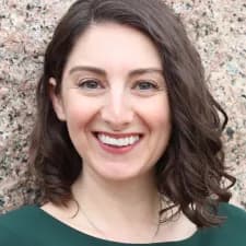 Headshot of Emily Margolis, a person with light skin, wavy shoulder-length brown hair, smiling.