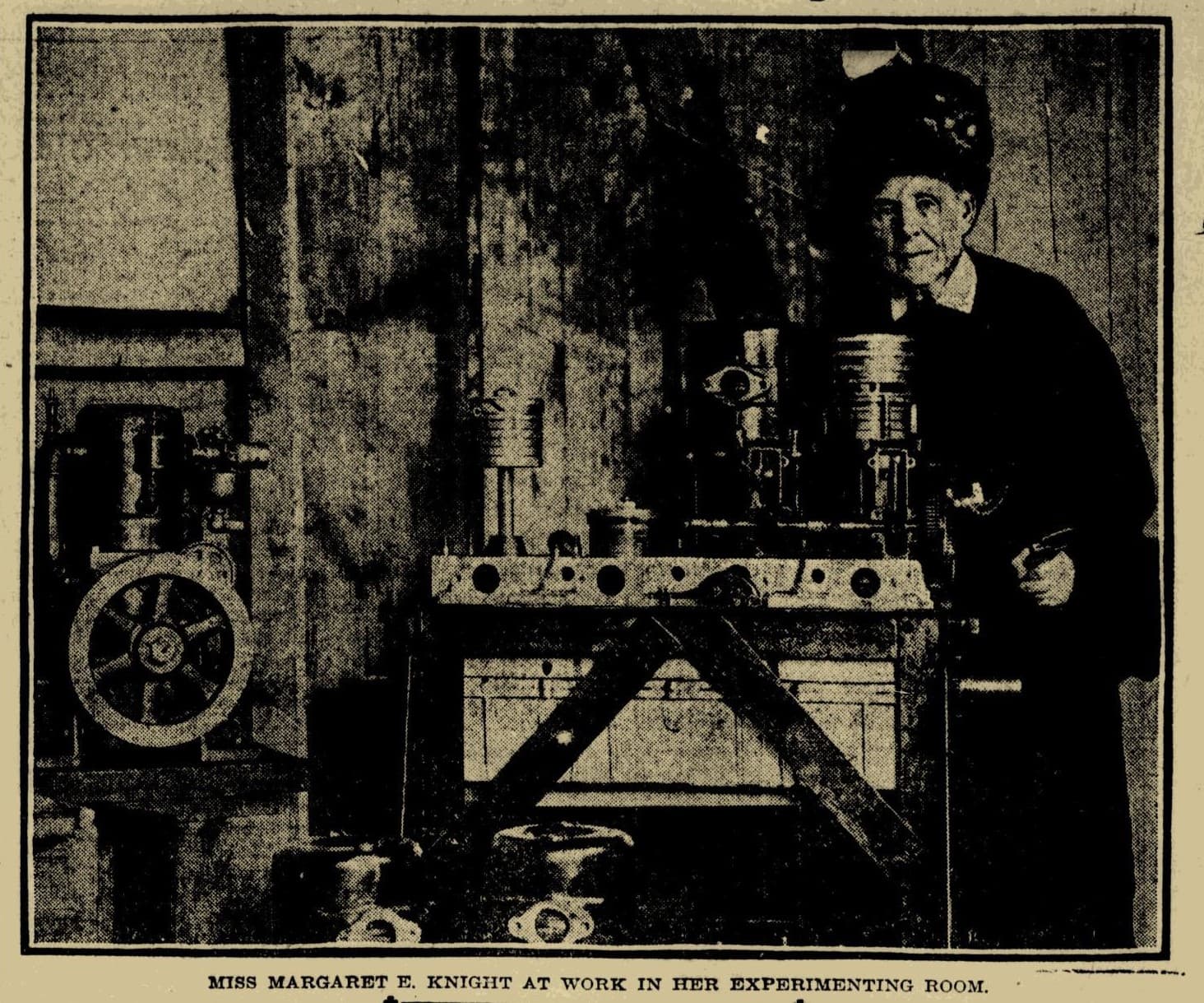 Old black and white newspaper photo of Margaret E. Knight standing behind the paper bag machine.  The headline reads: "First Woman Granted an American Patent is Still at Work on Ingenious Inventions"